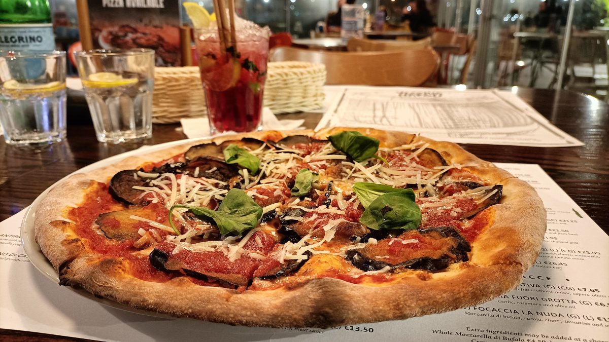 Close-up van een verse Italiaanse pizza die net uit de oven komt. Op tafel geplaatst, met drankjes op de achtergrond